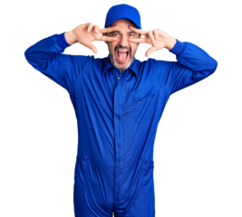 Middle age handsome man wearing mechanic uniform doing peace symbol with fingers over face, smiling cheerful showing victory