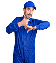 Middle age handsome man wearing mechanic uniform doing thumbs up and down, disagreement and agreement expression. crazy conflict