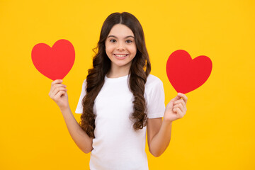 Teenage girl hold shape heart, heart-shape sign. Child holding a red heart love holiday valentine symbol, isolated on yellow background. Happy teenager, positive and smiling emotions of teen girl.