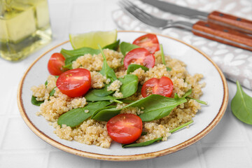 Delicious quinoa salad with tomatoes and spinach leaves served on white tiled table, closeup