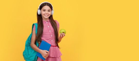 happy school teen girl in headphones carry backpack and workbook with apple for lunch. Banner of schoolgirl student. School child pupil portrait with copy space.