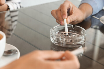 Woman putting out cigarette in ashtray at table, closeup