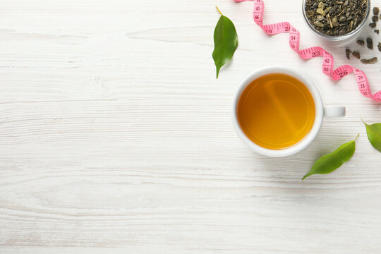Flat lay composition with herbal diet tea and measuring tape on white wooden table, space for text. Weight loss concept