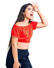 Fototapeta premium Brunette teenager girl wearing casual clothes very happy and smiling looking far away with hand over head. searching concept.
