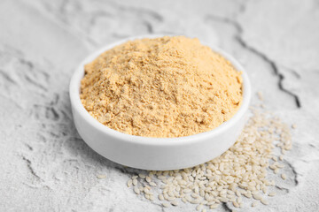 Sesame flour in ceramic bowl on white textured table, closeup