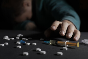 Addicted man reaching to drugs at black table, focus on syringe