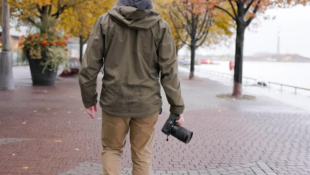 Photographer walking in an urban city setting during the fall season with professional mirrorless camera in hand view from behind