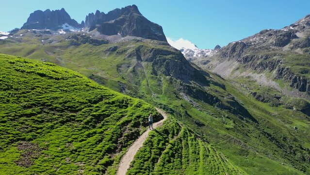 Young Adult Woman hikes trail in green valley in French Alps - Aerial Dolly Follow