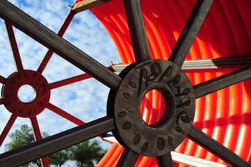 Large industrial steel spools hold orange conduit tubing for underground broadband fiber...