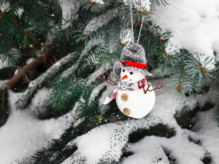 Christmas background, Snowman toy hanging on snow-covered branches of a Christmas tree on a snowy day