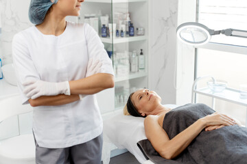 Cropped view of the cosmetologist woman looking at her senior female patient while standing