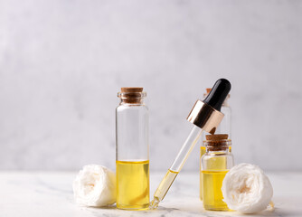 Dropper and three bottles with rose essential aroma oil and rose flowers on light  grey textured background. Selective focus is on left bottle. Place for text.