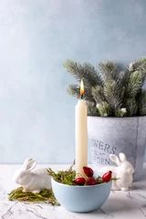 Foto auf Leinwand White burning candle, moss, briar berries,  white bunnies and Branches og Christmas tree in bucket on white marble background against blue  textured wall. Rabbit is symbool of 2023.. Selective focus.  © daffodilred