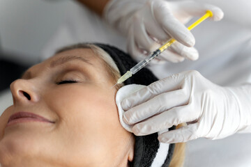 Senior woman attending beautician, having anti-aging injection at her face