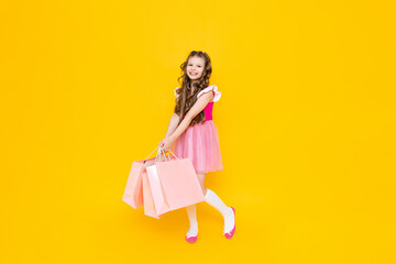 A little girl with full-length shopping. A fashionista after shopping on a yellow isolated background. Children's sale. The young princess is happy to make new purchases.