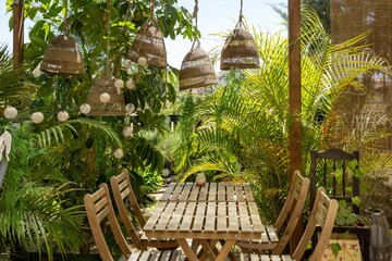 Wooden table with chairs and straw lamps in a wooden gazebo decorated with exotic plants