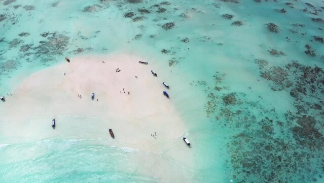 4K flying drone footage of boats on white sandbank coast with beautiful transparent rippled waves washing coral reefs atoll. Mnemba island, Zanzibar, Tanzania.Traveling in innocent Nature concept.