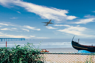 A bridge on the sea shore, a beautiful boat, an airplane flying in the sky, natural beauty.