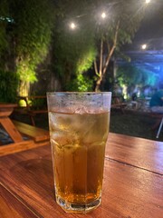 A glass of iced tea with ice cube on a wood table inside a restaurant.