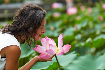 A young, beautiful woman is resting by the lotus pond. Portrait of a beautiful woman in a green park by a lotus pond with blooming lotuses