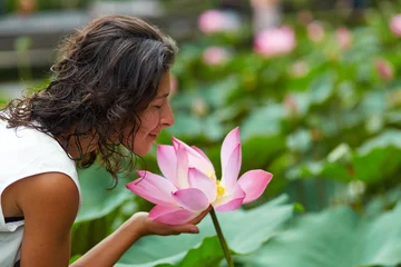 Schilderijen op glas A young, beautiful woman is resting by the lotus pond. Portrait of a beautiful woman in a green park by a lotus pond with blooming lotuses © Kate