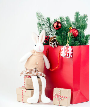 New Year's Eve photo with a red package with fir branches and Christmas gifts on which sits a rabbit. The photo can be used for postcards, calendars, flyers.