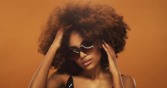 Studio portrait of young beautiful african woman with afro hair winking, wearing sunglasses
