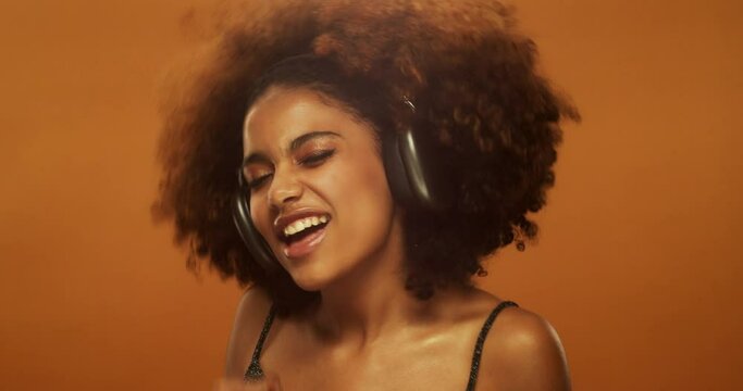 Beautiful african woman with afro hairstyle singing song, wearing headphones, isolated on brown studio background
