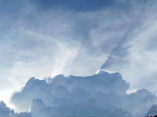 Amazing blue sky with puffy clouds. Thick ray of sun light coming out from behind one of the silver...