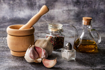 Oil can, peppercorn jar, wooden mortar, salt and garlic on a gray stone background, close-up.