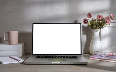 Fototapeta premium Feminine workspace with laptop, books, coffee cup and pink rose in vase. Blank screen for your advertise text.