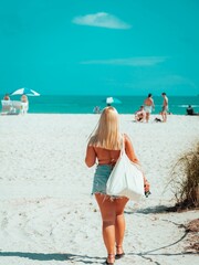 Back shot of a blonde woman with sea clothes walking on the sunny beach by the sea