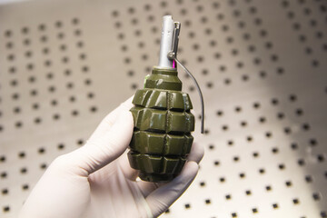 A hand in a rubber glove holds a grenade close-up