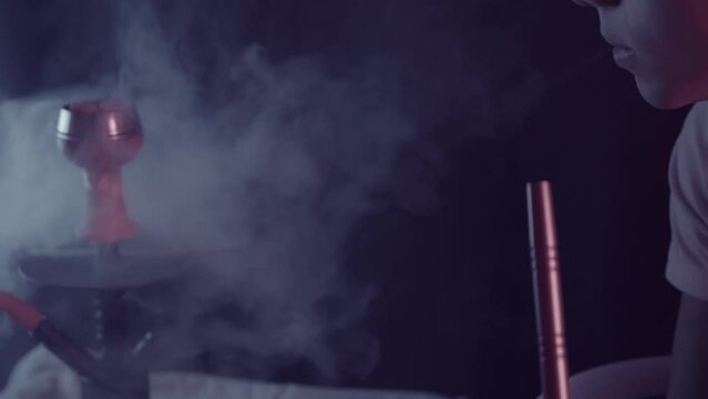 young man smoking a hookah while watching the smoke come out