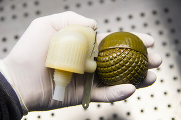 A man's hand in a rubber glove holds a disassembled grenade close-up
