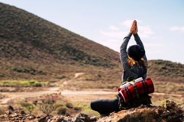 Back view of adventure woman doing yoga healthy position in front of a mountain in outdoor trekking...