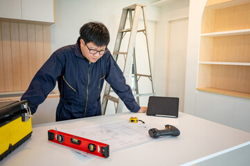 Home renovation or house remodeling concept. Asian male interior manual worker working with construction tools on countertop of new kitchen. Furniture assembler man installing cabinet and counter.