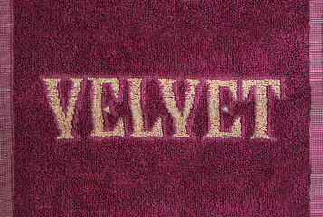 Fragment of a terry towel with the inscription Velvet light letters on a dark purple background