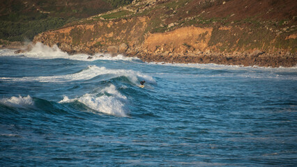 Unidentified surfers riding the rolling waves at Sennen Cove in Cornwall during late sunset