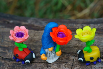 A toy gnome and a ladybug with flowers. Fabulous scenery. Plasticine figurines.