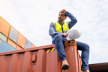 A tired male worker taking a break and rest sitting from hard work in the cargo container shipping...