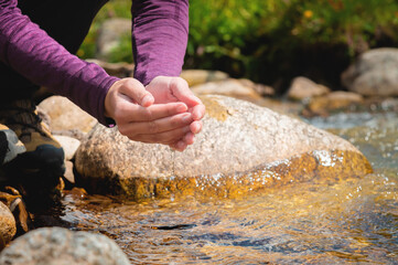 female hands close-up draw water from a mountain stream to quench thirst, drink from a clean source of water. tourist on a hot sunny day