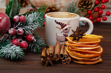 Obraz na płótnie Canvas A cup of hot drink on a wooden table among Christmas decor and spicy spices. Christmas card.