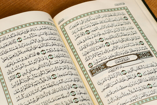 Showing Quran On Wood Table Indonesia - November 26, 2022 An open page of the Quran showing Surah Yusuf, on brown background. Quran is an Islamic Holy Book. Selective focus.