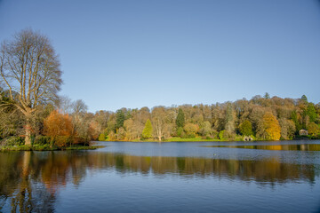 Fototapeta na wymiar autumn afternoon sunshine illuminates woodland and island in a lake