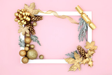 Christmas background border on pink with gold tree bauble decorations, symbols of the holiday season and snow covered fir with white frame. 