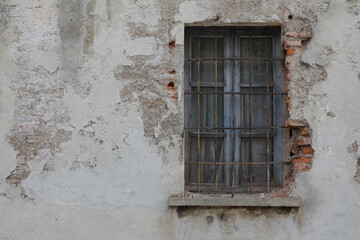 Fototapeta na wymiar Old and cracked house wall with window, frame closed and with lattice, damaged bars, wall with bricks