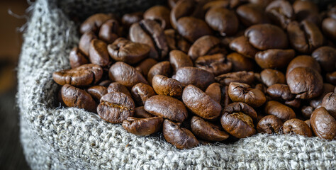 Сlose-up of bag of coarse canvas of coffee beans. Background with dark wood texture.