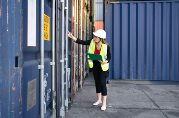 Female foreman supervisor wears safety hardhat inspecting container cargo at warehouse storage terminal. Industrial engineer woman works outdoors at international import export distribution facility.