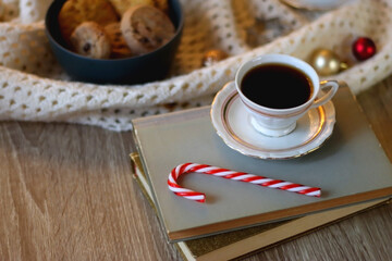Cups of tea or coffee, bowl of cookies, soft blanket, lit candles, books and various Christmas decorations on the table. Selective focus.